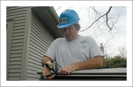 contractor with hardhat holding pliers pinching something together in front of home with new siding