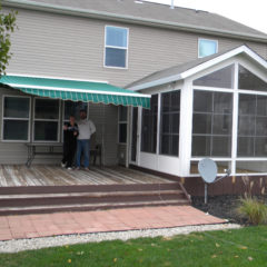 back deck of home with a couple standing under a green and white oning beside a sunroom