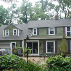 home with green siding and brown shutters around new windows with trees all around yard